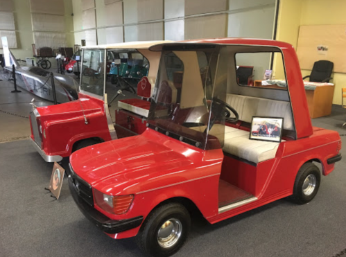 Two vintage red golf carts displayed indoors, featuring unique designs and a small screen showing images.