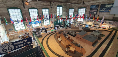 Aerial view of a model train display in a museum, featuring flags and informational displays about Route 66.