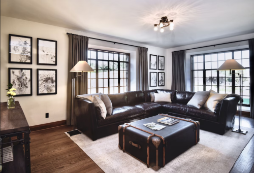 Cozy living room with a leather sectional, coffee table, artwork on the walls, and large windows letting in natural light.