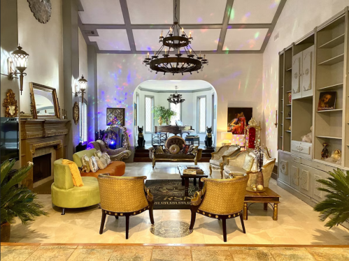 A spacious, elegantly decorated living room with colorful lighting, ornate furniture, and a cozy fireplace.
