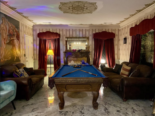 A cozy room with a pool table, plush sofas, and elegant decor, featuring patterned wallpaper and warm lighting.