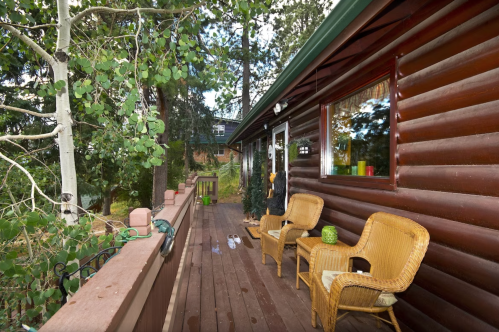 A wooden deck with two chairs, surrounded by trees and a cabin in the background.