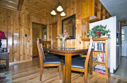 Cozy wooden dining area with a table, chairs, and a decorative plant, featuring warm lighting and rustic decor.