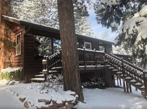 A cozy log cabin surrounded by snow-covered trees and a wooden staircase leading to the entrance.