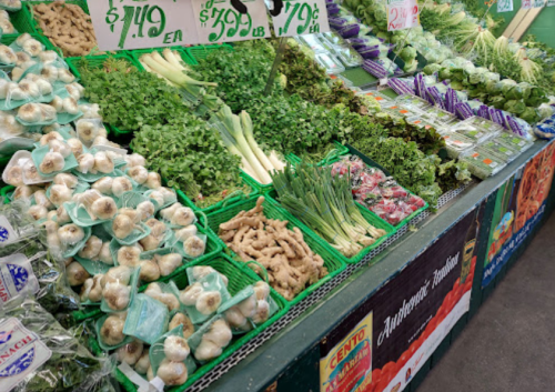 A vibrant market display featuring fresh vegetables, including garlic, green onions, and various leafy greens.