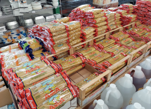 A display of stacked pasta packages in red and yellow packaging, arranged on wooden pallets in a store.