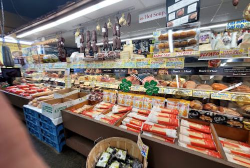 A vibrant deli display featuring various meats, breads, and pastries, with colorful signage and products neatly arranged.