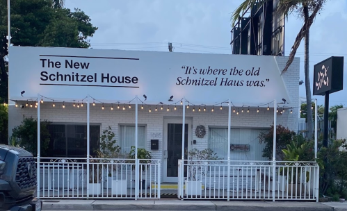 Exterior of "The New Schnitzel House," featuring a sign and outdoor seating, with a quote about its predecessor.