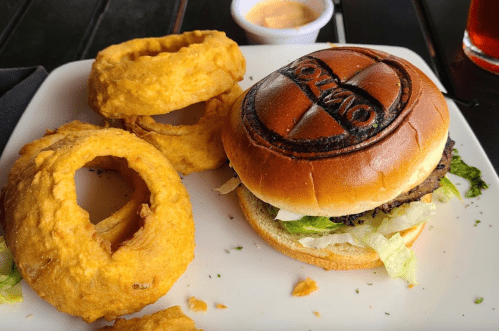 A plate featuring a burger with a branded bun and crispy onion rings, accompanied by a dipping sauce.