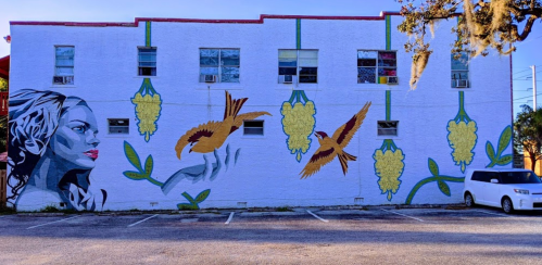 A colorful mural on a building featuring a woman's face, birds, and yellow flowers against a white background.