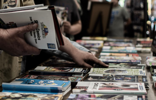 A person browsing comic books at a table filled with various titles and colorful covers.