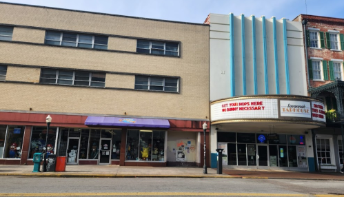 A street view of a building with a marquee sign and storefronts, featuring a colorful facade and clear blue sky.