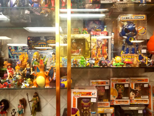 A display case filled with various action figures and collectibles, including toys from Digimon, Sonic, and other franchises.
