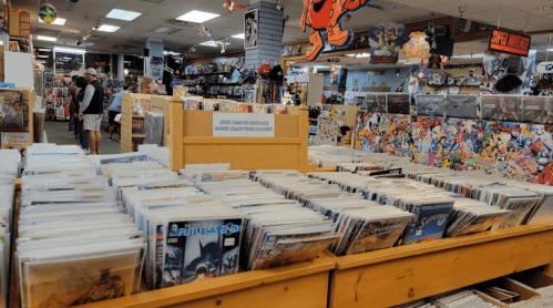 A comic book store interior with shelves of comics, posters on the walls, and customers browsing.