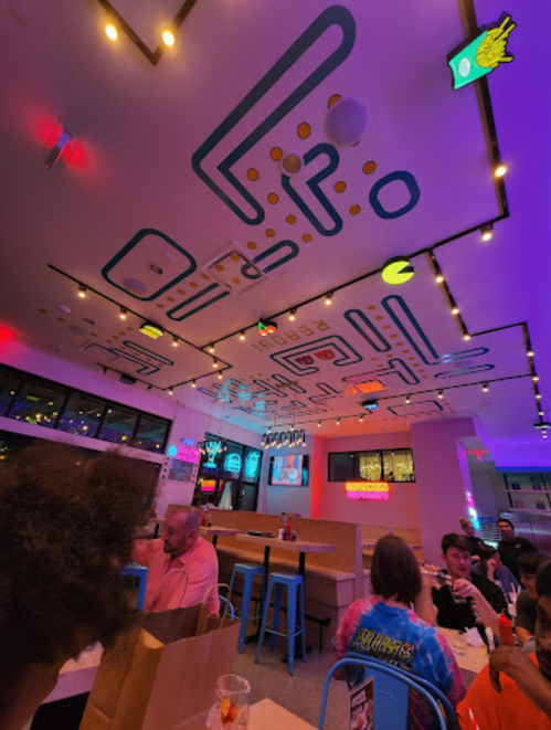 Colorful restaurant interior with a Pac-Man themed ceiling, neon lights, and lively dining atmosphere.