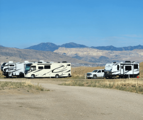 Two RVs parked on a dirt road with mountains in the background under a clear blue sky.