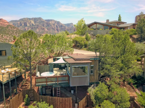 A modern cabin nestled among trees, with a hot tub and stunning mountain views in the background.