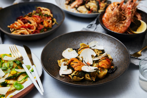 A beautifully arranged table with various dishes, including pasta, seafood, and a salad, showcasing vibrant colors and textures.