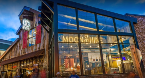 A modern building with large glass windows, featuring a sign that reads "Moscow." People walk by in the foreground.