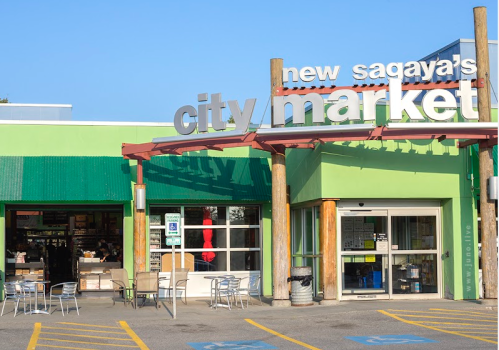 Exterior of New Sagaya's City Market, featuring a green facade and outdoor seating area under clear blue skies.