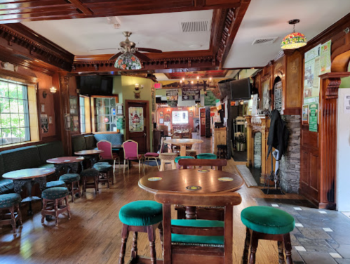 Interior of a cozy pub with wooden decor, green seating, and tables, featuring a warm, inviting atmosphere.