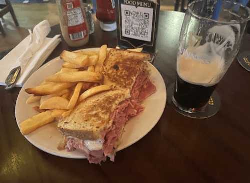 A plate with a sandwich filled with meat, fries, and a pint of dark beer on a wooden table.