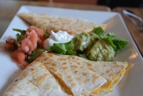 A plate of quesadillas with cheese, served with guacamole, sour cream, and a side of pico de gallo and salad.