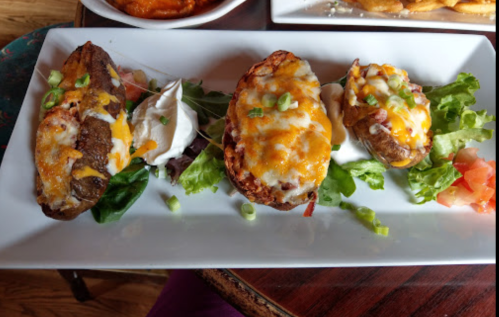 Three loaded potato skins topped with cheese, sour cream, and green onions, served on a bed of lettuce and tomatoes.