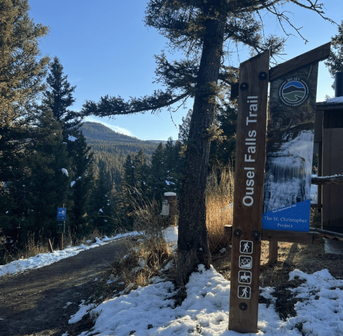 Sign for Ousel Falls Trail with snowy ground and trees in the background, under a clear blue sky.