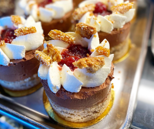 Delicious chocolate mousse cakes topped with whipped cream, fruit jam, and crunchy caramel pieces on a golden base.