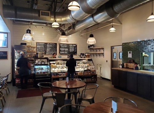 A cozy café interior with a display case, menu boards, and tables. Two people are at the counter.