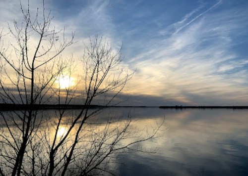 A serene lake at sunset, with silhouetted trees and colorful clouds reflecting on the water's surface.
