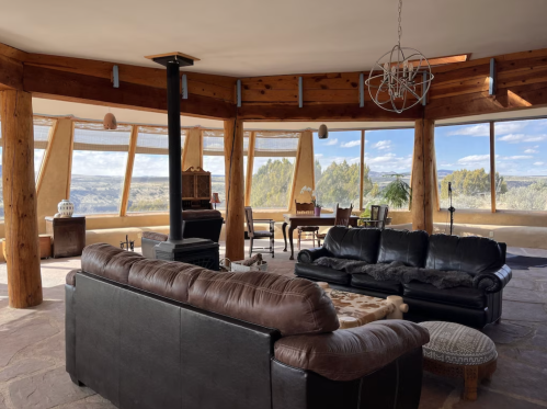 Spacious interior with large windows, wooden beams, and cozy seating, offering a scenic view of the outdoors.