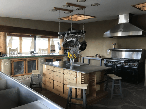 A modern kitchen with a wooden island, stainless steel appliances, and large windows, featuring a vase of flowers.