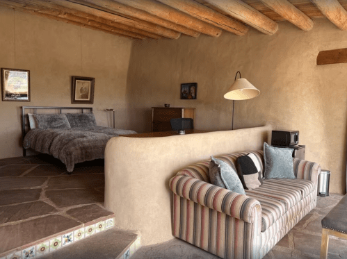 Cozy bedroom with a bed, striped sofa, and rustic decor, featuring wooden beams and stone flooring.