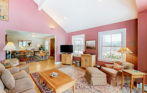 Cozy living room with pink walls, a wooden coffee table, and large windows showcasing a snowy landscape outside.