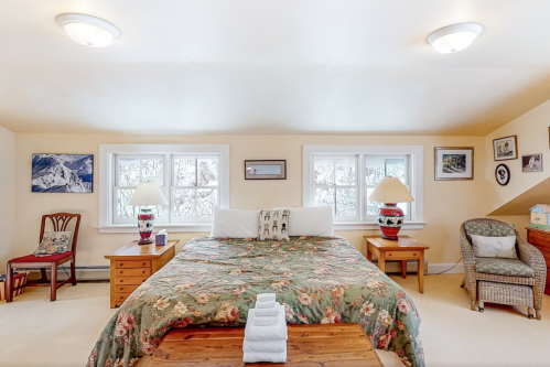 Cozy bedroom with a large bed, floral bedding, two lamps, and artwork on the walls, featuring a warm, inviting atmosphere.