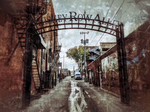 A weathered alleyway entrance with "Whiskey Row Alley" sign, flanked by brick buildings and power lines.