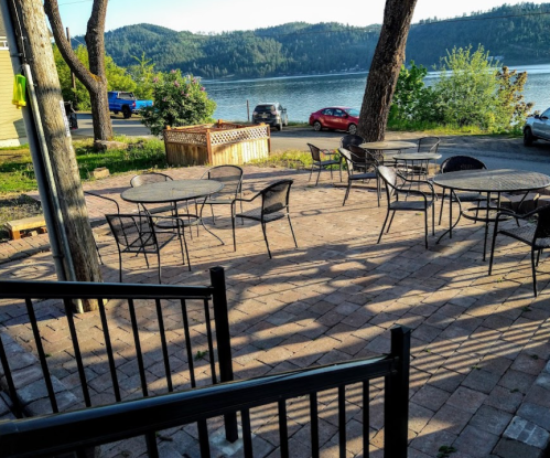 Outdoor seating area with metal tables and chairs, overlooking a lake and mountains in the background.