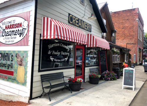 A charming creamery with red and white striped awnings, flowers, and a sign indicating open hours.