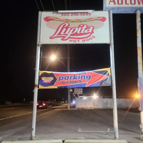 Sign for "Lypita Hot Dogs" with a banner stating "Parking on back" at night.