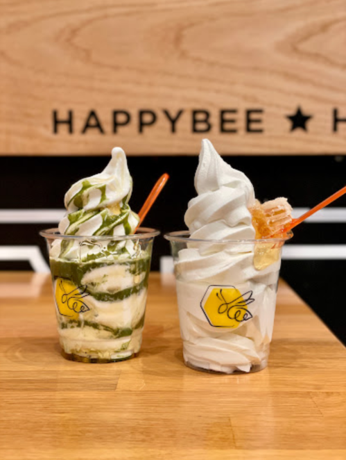 Two cups of soft serve ice cream: one with green tea swirl and the other topped with honeycomb, set against a wooden background.