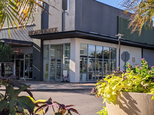 A modern building with large glass windows, surrounded by colorful plants and a clear blue sky.