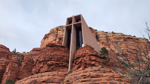 A modern building perched on red rock formations against a cloudy sky, showcasing unique architectural design.