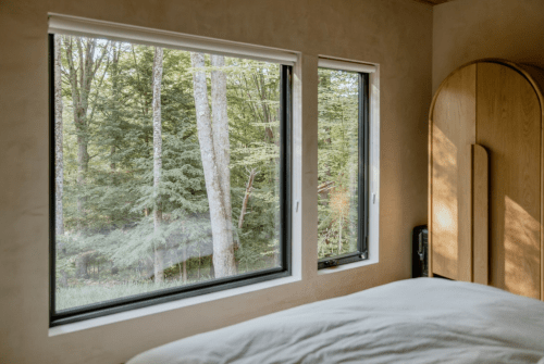 Cozy bedroom with a bed and large windows showcasing a serene forest view.