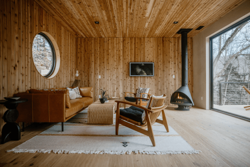 Cozy wooden living room with a circular window, modern furniture, and a fireplace, creating a warm atmosphere.