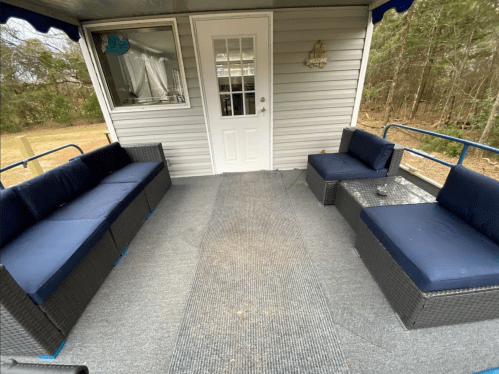 A cozy outdoor seating area with navy blue couches and a glass table, leading to a white door. Surrounded by trees.