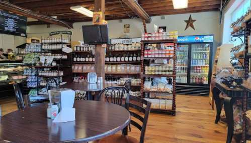 A cozy deli interior with wooden tables, shelves of products, and a display of drinks in a bright, inviting space.