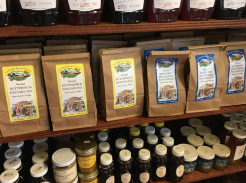 A wooden shelf displaying various bags of buttermilk pancake mix and jars of honey.