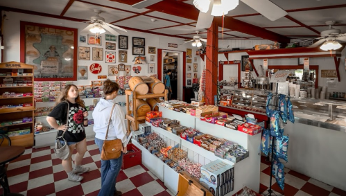A vintage candy shop with colorful displays, wooden barrels, and nostalgic decor. Two customers browse the selection.